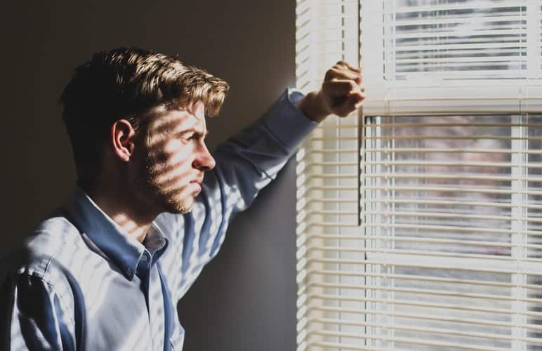 A sad adult man staring out a window.